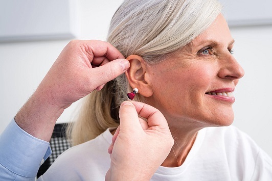 Ältere Frau bekommt ein modernes Hörgerät ins Ohr eingesetzt, Hörgeräte-Anpassung.